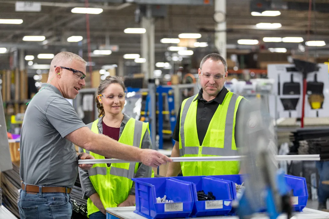Three factory workers inspecting a long component at a production workstation.