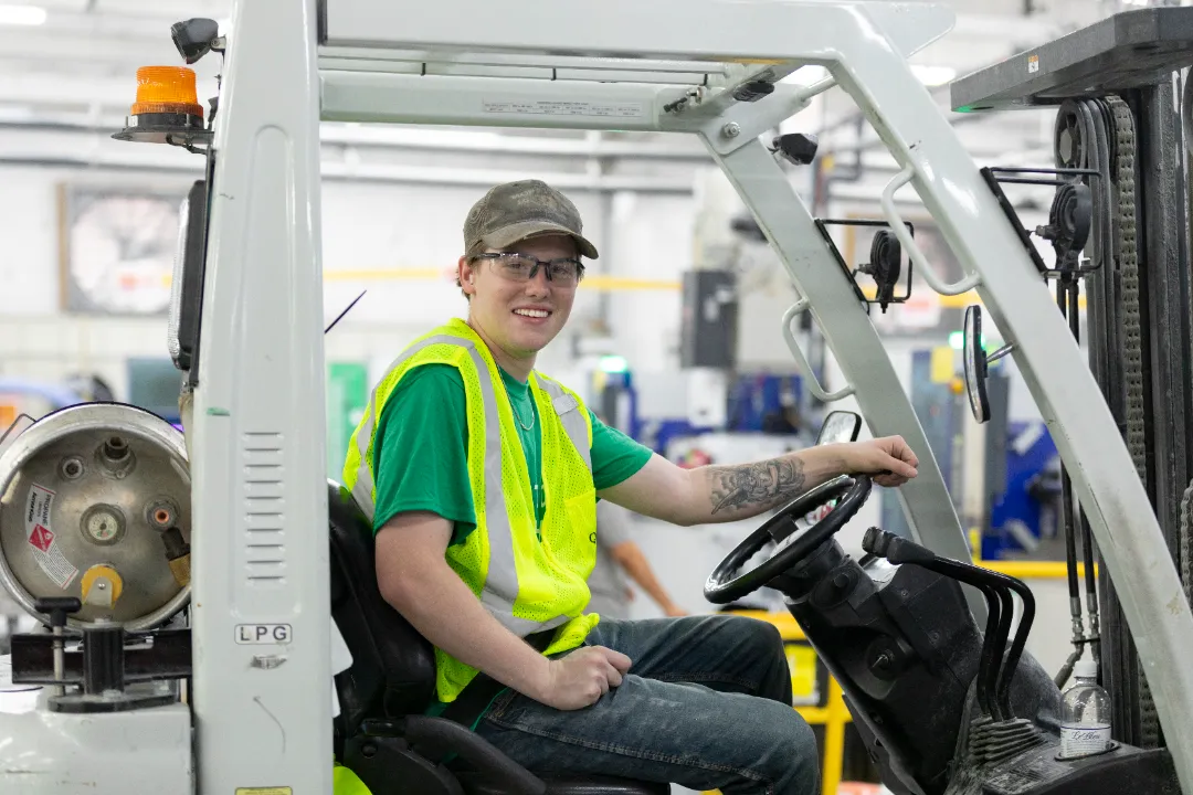 Factory worker wearing a high-visibility vest and safety glasses while operating a forklift.