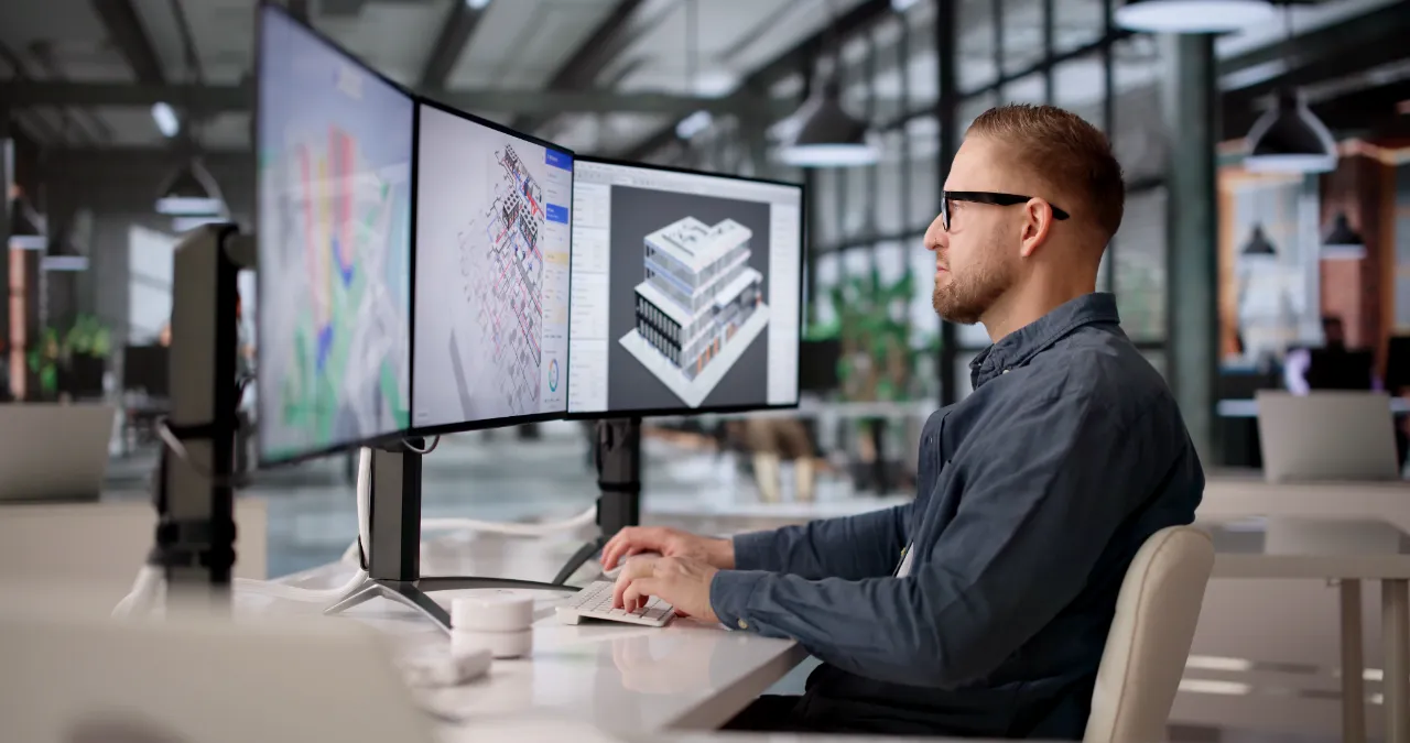 Architect working on a 3D building model across three computer monitors in a modern office.