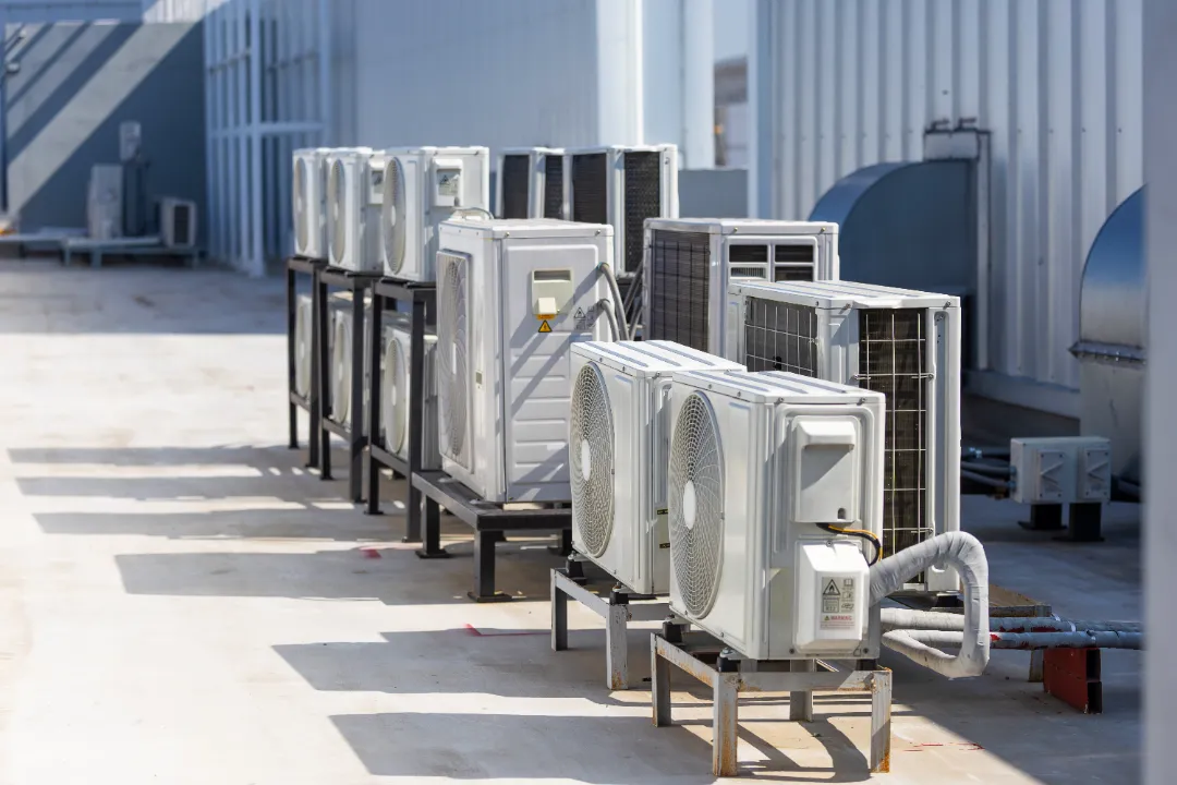 Rows of outdoor air conditioning units installed on raised frames beside a commercial building.